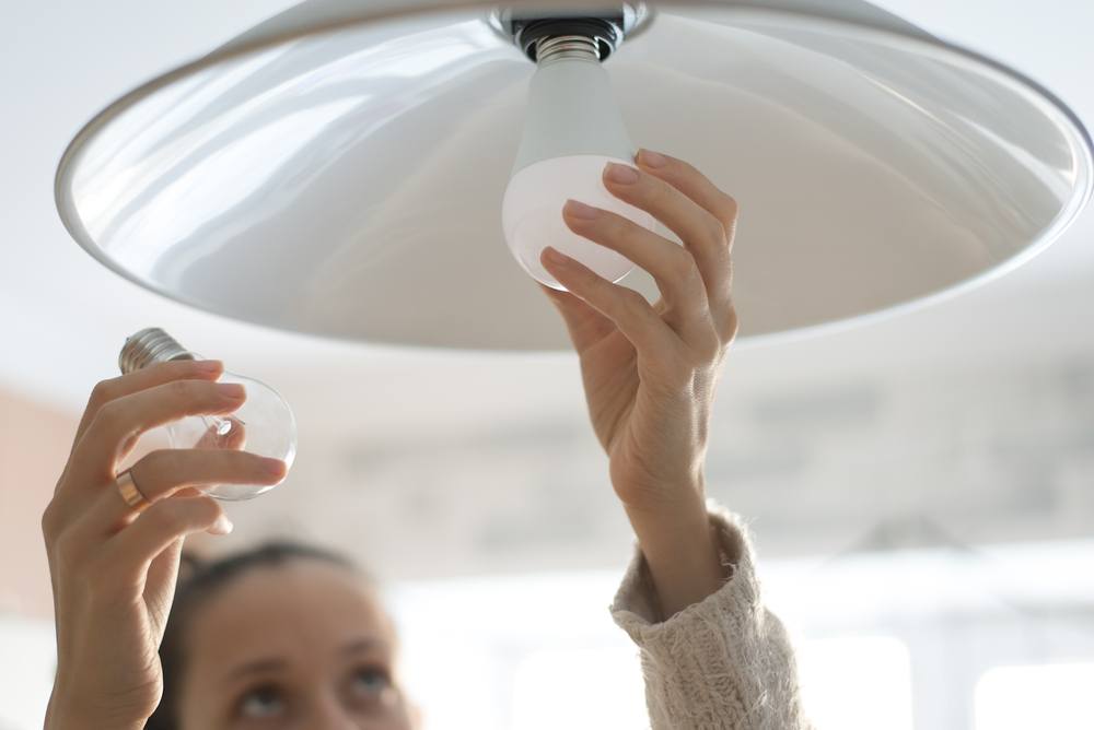 A woman changes out an incandescent light bulb for an energy-efficient LED bulb