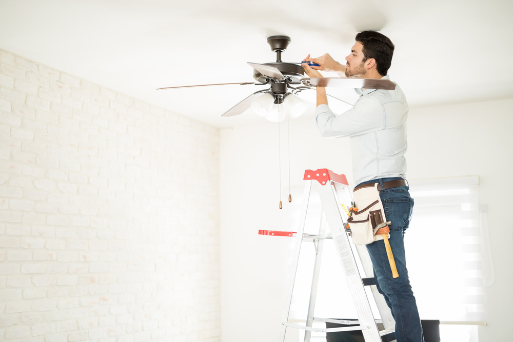 A handyman installs a ceiling fan in a home